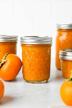 several jars filled with orange colored food sitting on top of a white counter next to tomatoes