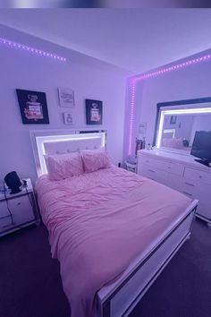 a bed with pink comforter and pillows in a room that has purple lights on the walls