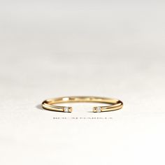 a gold ring with two small diamonds on it's side, sitting on a white surface