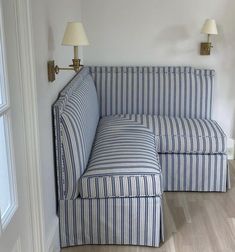 a blue and white striped couch sitting in a living room next to a lamp on the wall