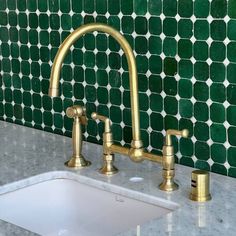 a kitchen sink with two faucets in front of a green tiled wall