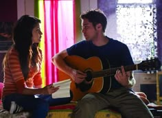 a man sitting next to a woman holding a guitar