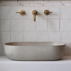 a bathroom sink with two brass faucets on the wall and white tile behind it