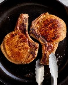 two steaks are being cooked in a cast iron skillet with tongs on the side