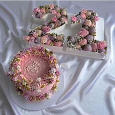 a cake with pink frosting and flowers on it next to a box of cupcakes