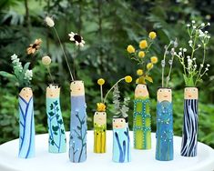 a group of wooden dolls sitting on top of a white table next to flowers and plants