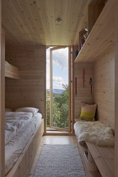 two beds in a small room with wooden walls and floor to ceiling windows looking out onto the woods