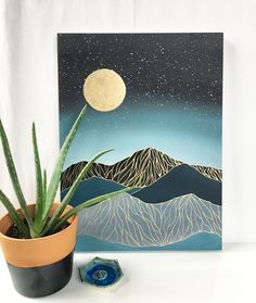 a potted plant sitting on top of a table next to a painting with mountains in the background