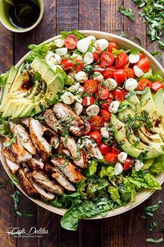 a salad with chicken, tomatoes, avocado and lettuce on it