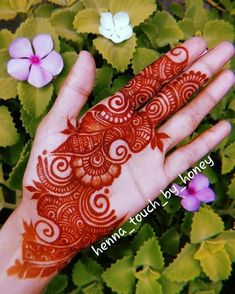 a hand with henna painted on it next to some purple flowers and green leaves