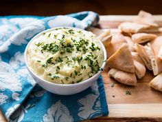 a bowl of mashed potatoes on top of a cutting board next to pita chips