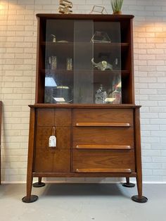 an old wooden cabinet with glass doors and drawers on wheels in front of a white brick wall