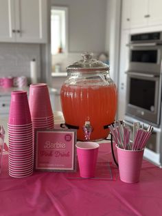 pink party supplies on a kitchen table with silverware and cups in front of it