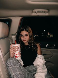 a woman sitting in the back seat of a car holding a cup