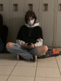 a person sitting on the ground wearing a face mask while looking at their cell phone