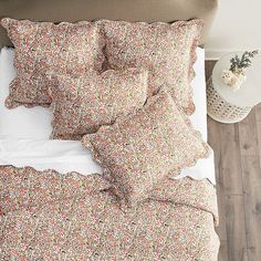 a bed with floral sheets and pillows on top of it, next to a night stand