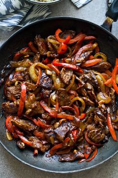 a skillet filled with meat and vegetables on top of a table next to silverware