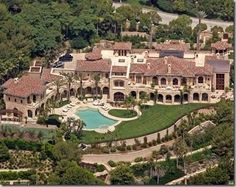 an aerial view of a mansion with a pool in the foreground and trees surrounding it