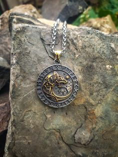 a silver and gold necklace with an image of a dog on it sitting on top of a rock