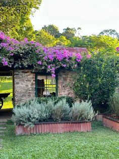 an old stone house with purple flowers growing on it's roof and garden area