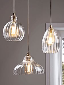 three clear glass pendant lights hanging from a ceiling in front of a white wall and window