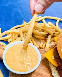 a person dipping cheese into a hamburger with fries