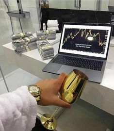 a person is holding a gold cup in front of a laptop and stacks of money