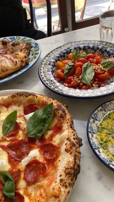 three plates with pizza and salad on them sitting on a table in front of a window