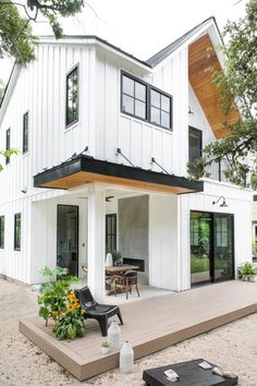 a white house with black trim and wood accents on the roof, covered in plants