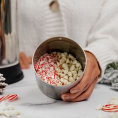 a person holding a metal bowl filled with candy canes and marshmallows