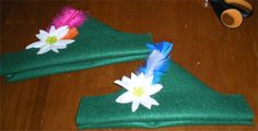 two pieces of cloth with flowers and feathers on them sitting on a wooden floor next to scissors