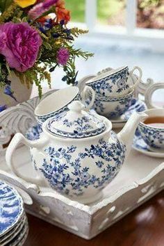 a blue and white tea set sitting on top of a table next to a vase filled with flowers