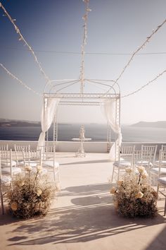 an outdoor ceremony setup with white chairs and flowers on the aisle, overlooking the ocean