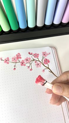 a hand holding a brush near a notebook with pink flowers on it