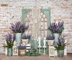 purple flowers are in vases next to an old wooden door and brick wall with shutters