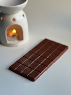 a chocolate bar sitting next to a white vase with a lit candle in the middle