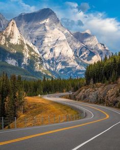 an empty road in the mountains with snow on the mountain tops and trees around it