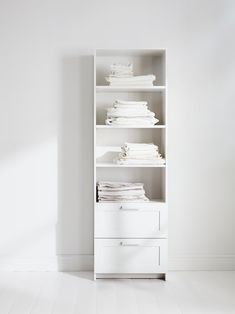 a white bookcase with folded clothes on the top and bottom shelves, against a white wall