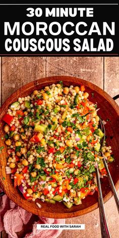 a wooden bowl filled with corn and vegetables on top of a table next to two spoons