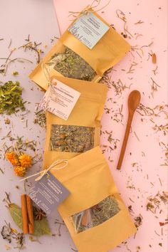 herbs and spices are laid out on top of yellow envelopes next to a wooden spoon