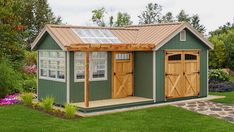 a small green shed with wooden doors and windows on the roof is shown in front of some flowers