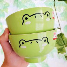 two green bowls with faces drawn on them in front of a wallpapered background