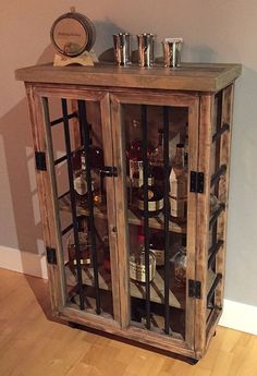 a wooden cabinet filled with liquor bottles on top of a hard wood floor next to a wall