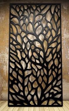 an intricate metal screen with leaves on it in front of a wooden floor and wall