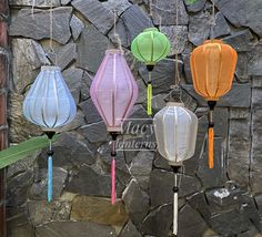 five colorful lanterns hanging from strings in front of a stone wall