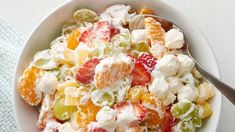 a white bowl filled with fruit salad on top of a blue and white towel next to a spoon