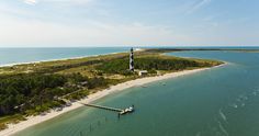 an aerial view of the ocean with a lighthouse in the distance and boats on the water