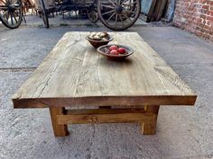 a wooden table with two bowls of fruit on it and an old wagon in the background