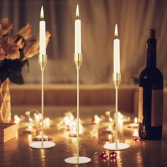 three candles are lit in front of a bottle of wine and some flowers on the table