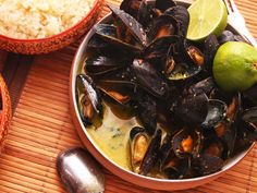 a bowl filled with mussels next to rice and lime